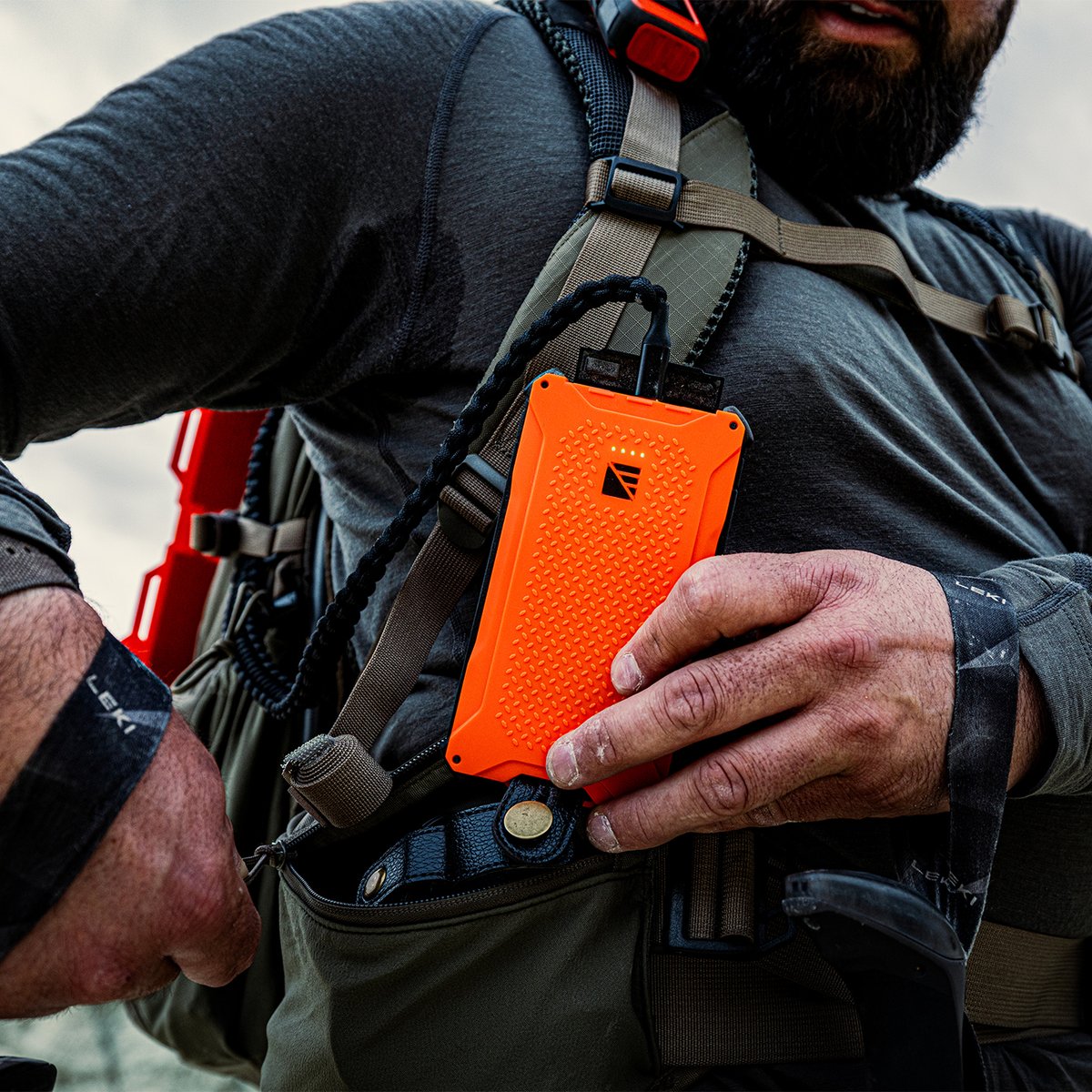 A hiker slides an orange Dark Energy Poseidon power bank into a pocket on his backpack shoulder strap.