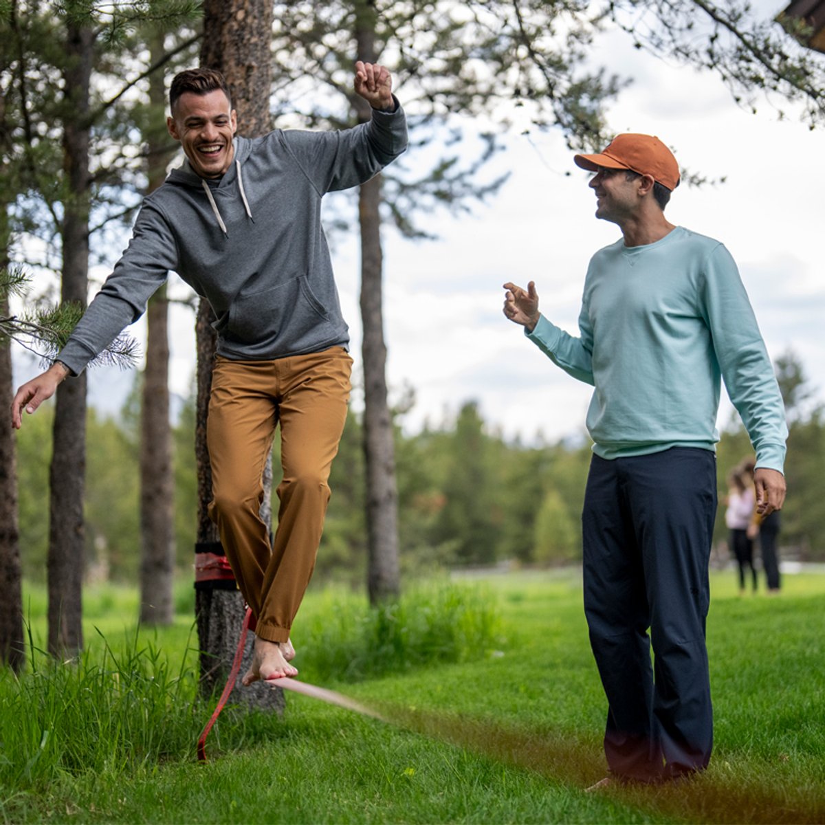 A man wearing Ferrosi pants walks along a Slackline, while another man watches from the side.