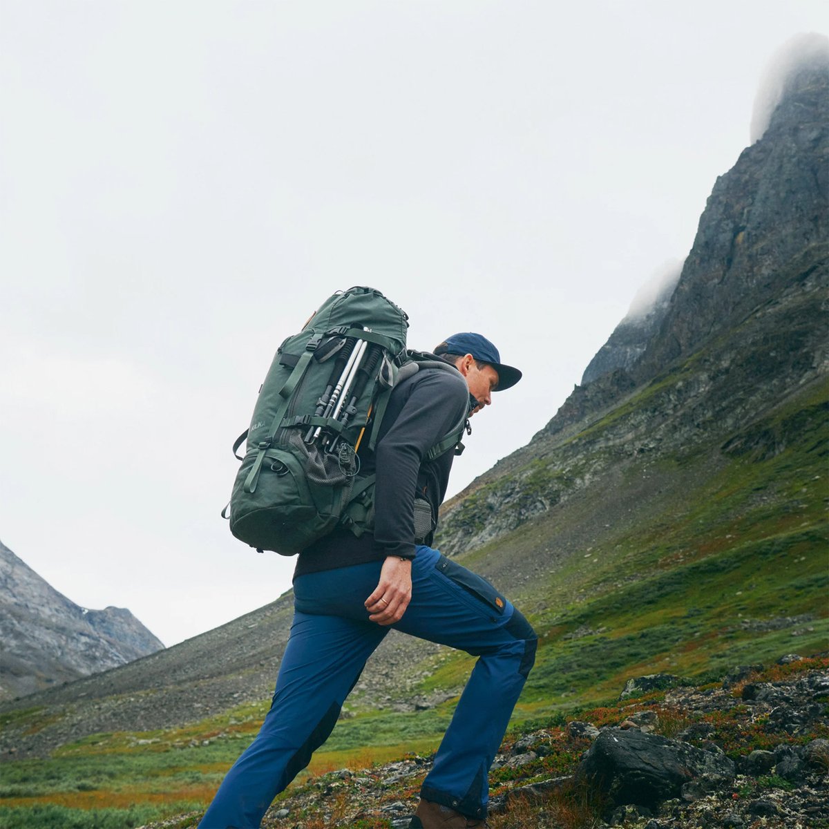 A man wearing Fjallraven Keb treks across a green mountainous landscape.