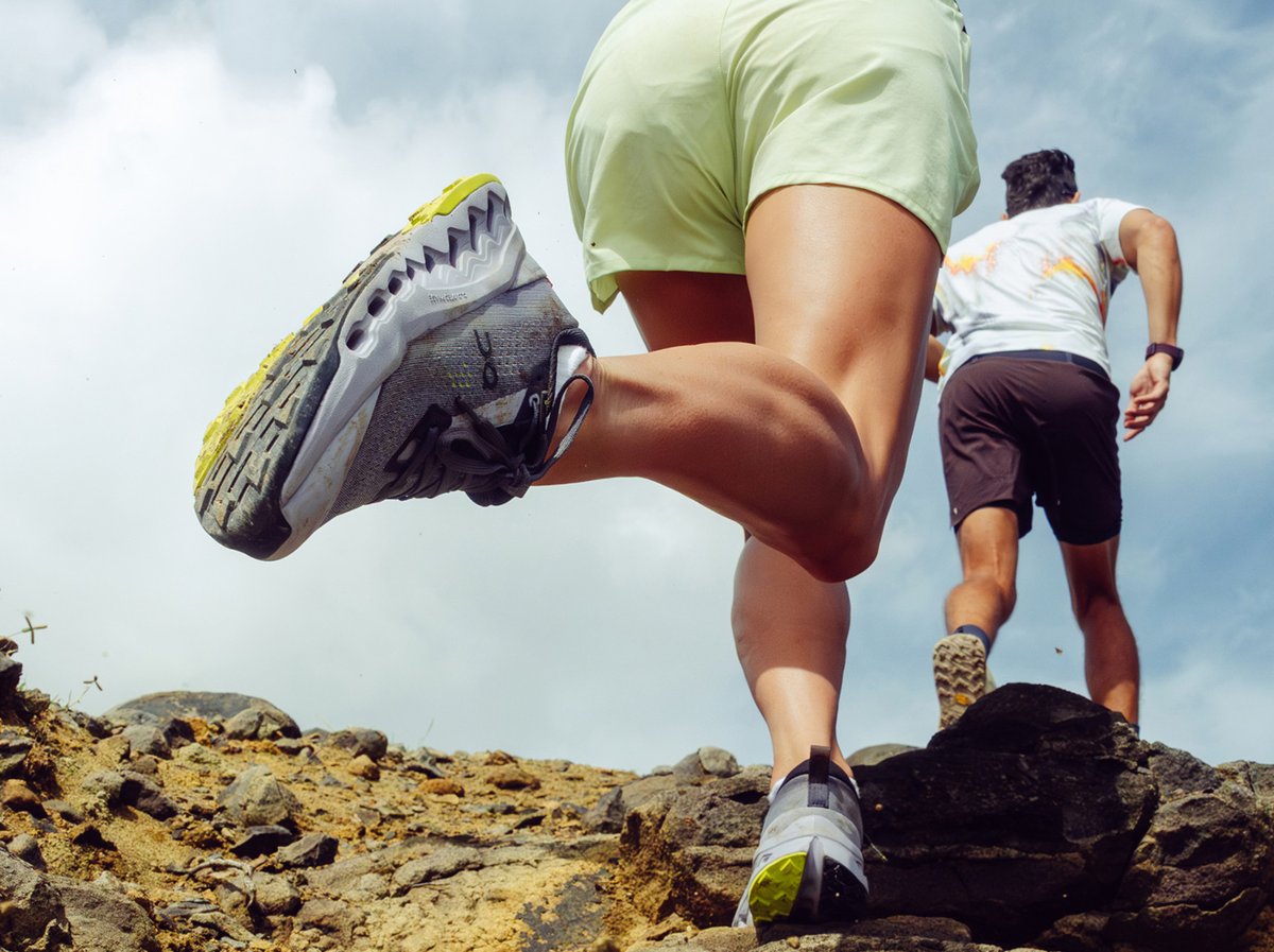 Two people run down a trail. The camera is close to the back runner’s shoe.