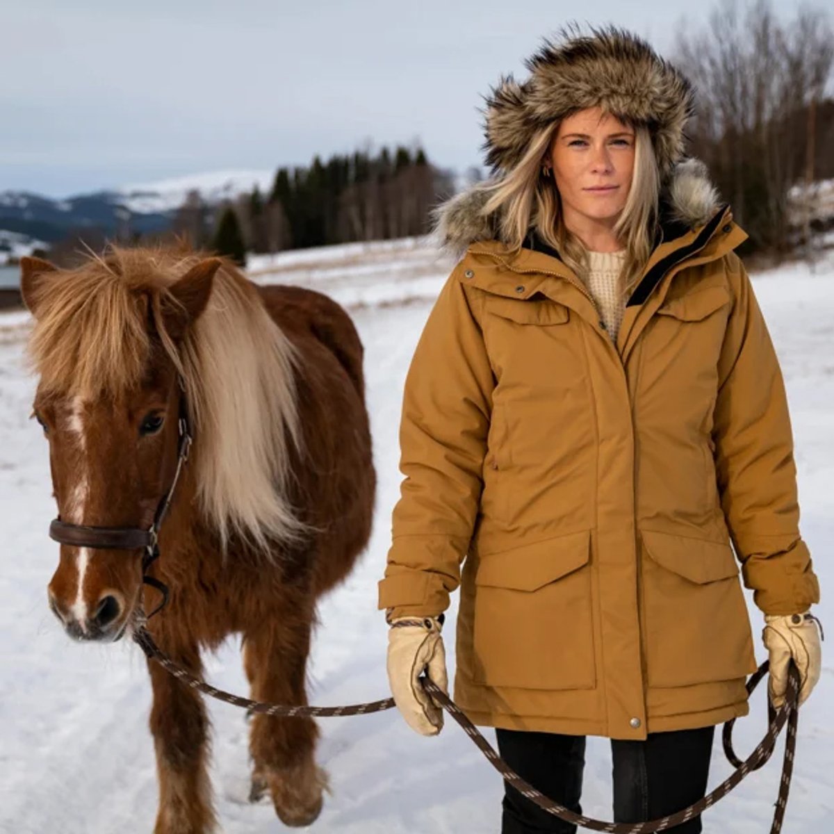 A woman puts on the Fjallraven Nuuk parka against a snowy backdrop.