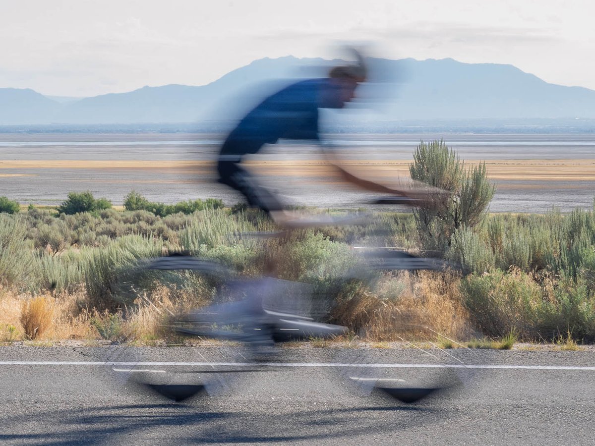 Motion-blurred cyclist riding the ENVE SES 6.7 PRO wheelset along a desert road with mountains in the background.