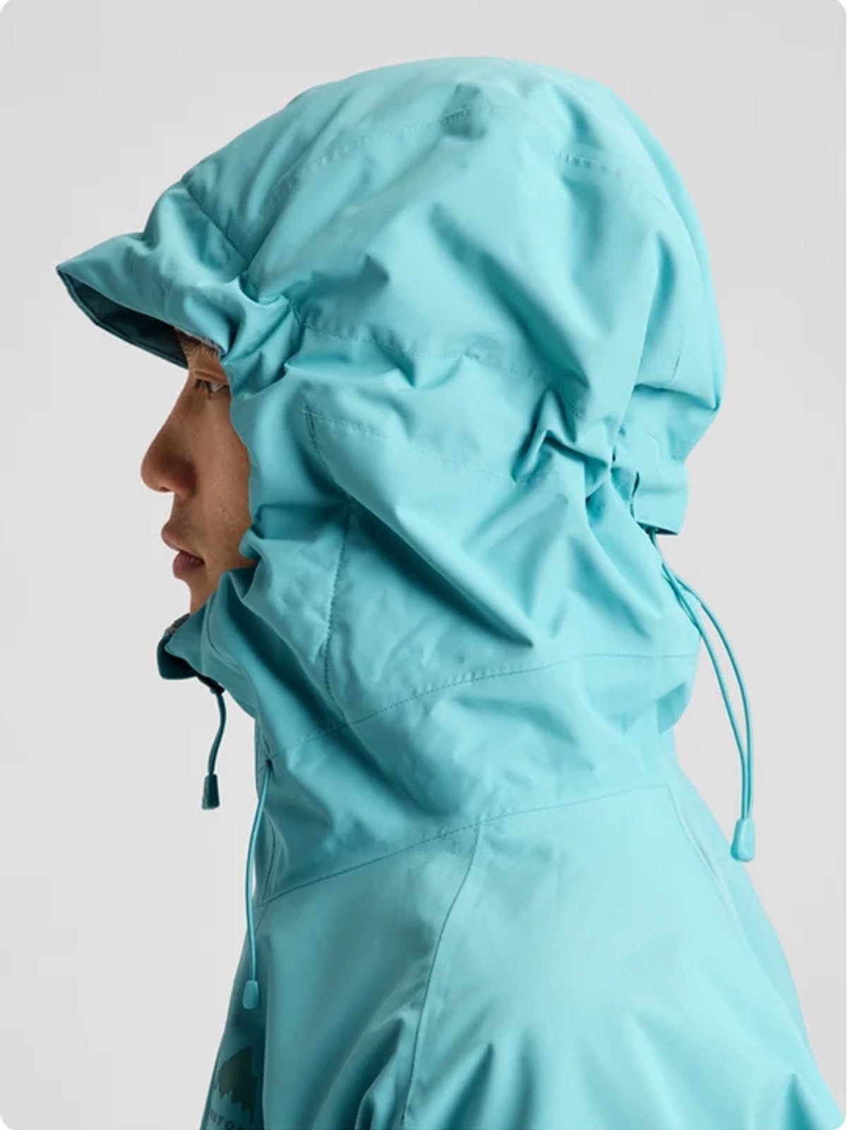 Light blue waterproof rain jacket with attached hood and drawstring closure on a model shown in side profile view.