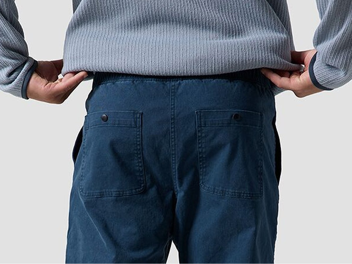 Close-up of a person wearing blue workwear-style pants with hands resting on the waistband.