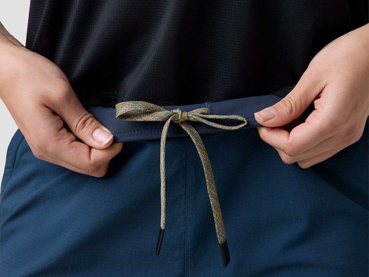 Detail of person wearing ripstop bottoms flipping front pull-on waistband inside out to show internal drawcord tie.