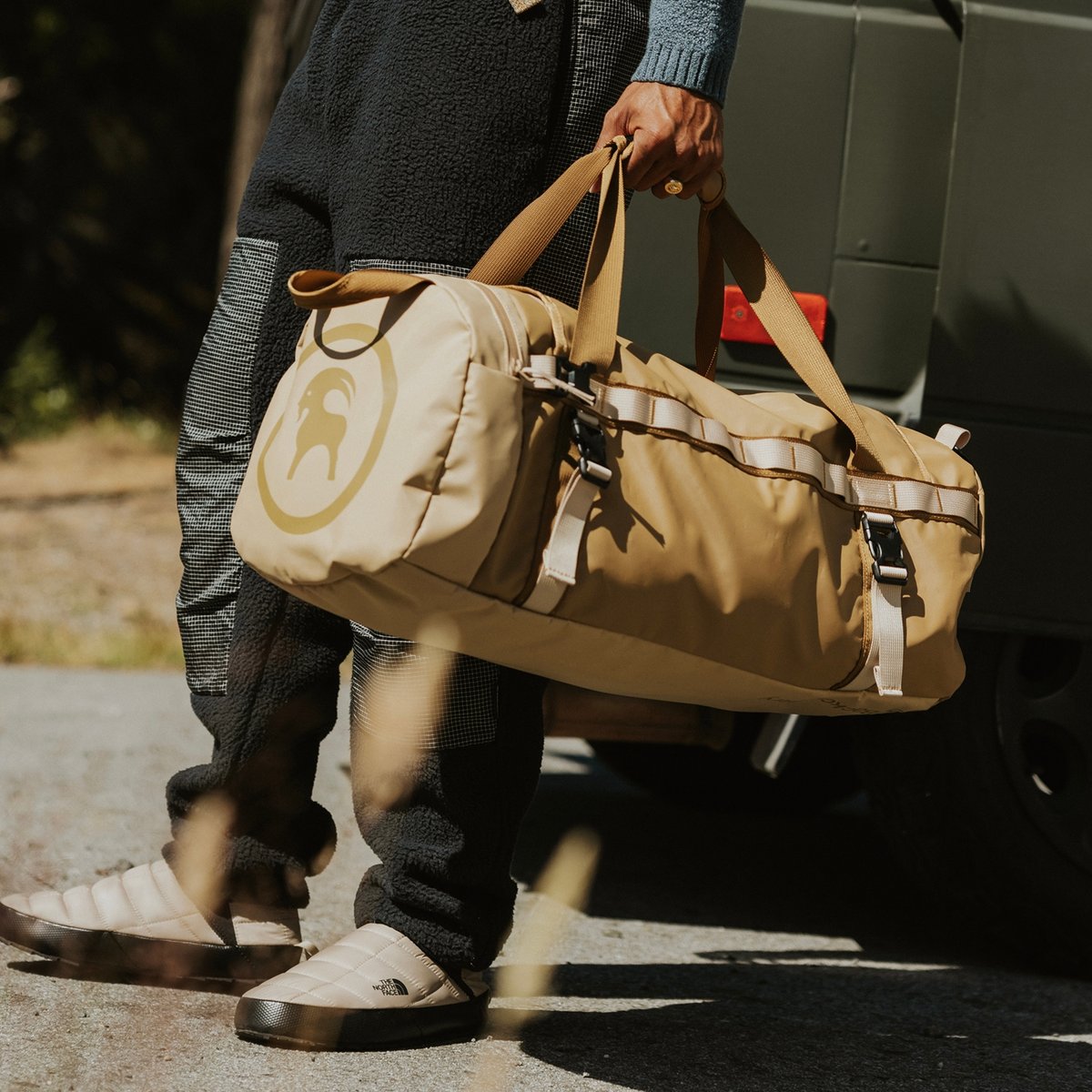 A person in a lounge outfit carries a Backcountry duffle bag.
