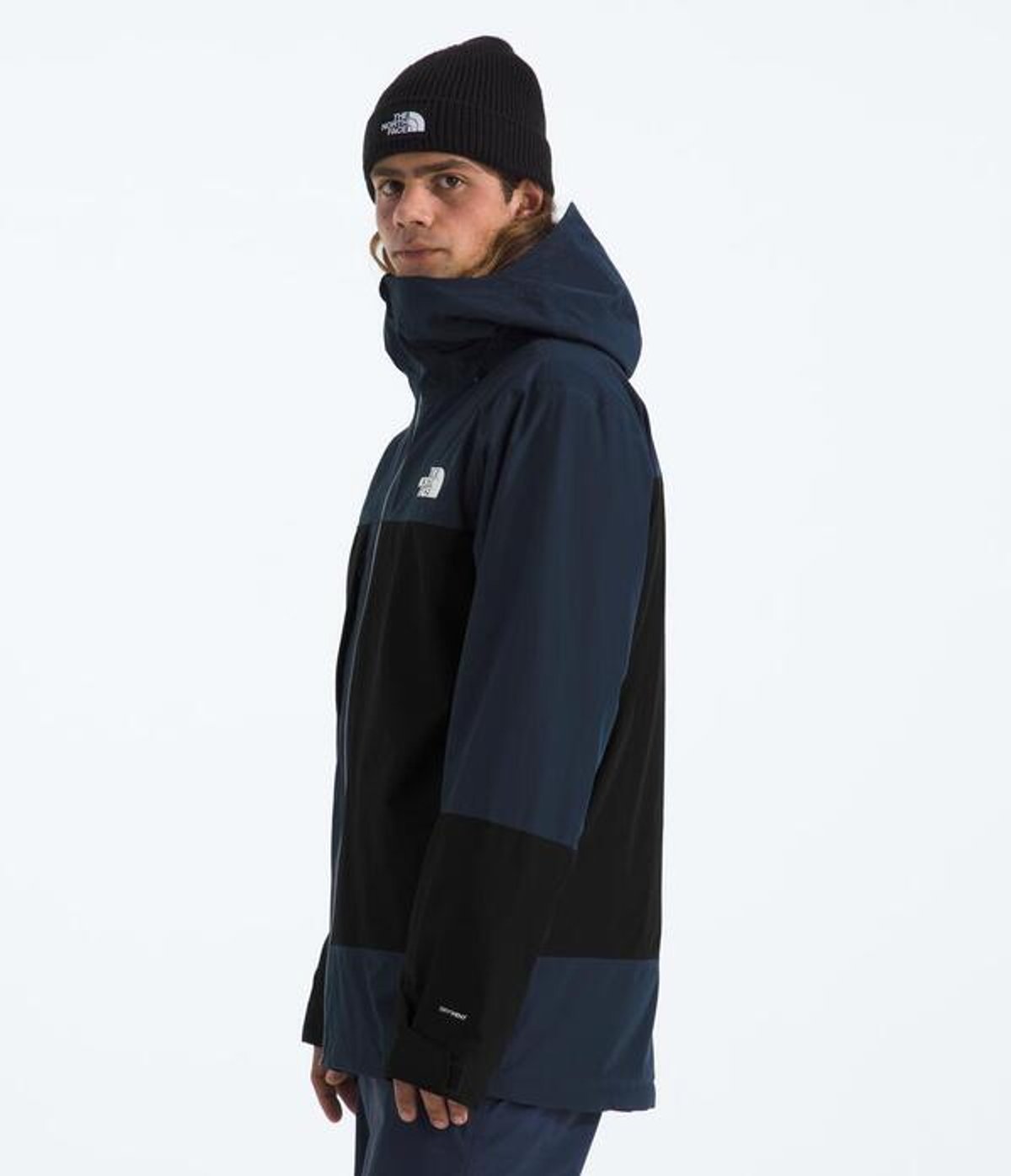 Person standing facing sideways wearing snow pants and jacket.