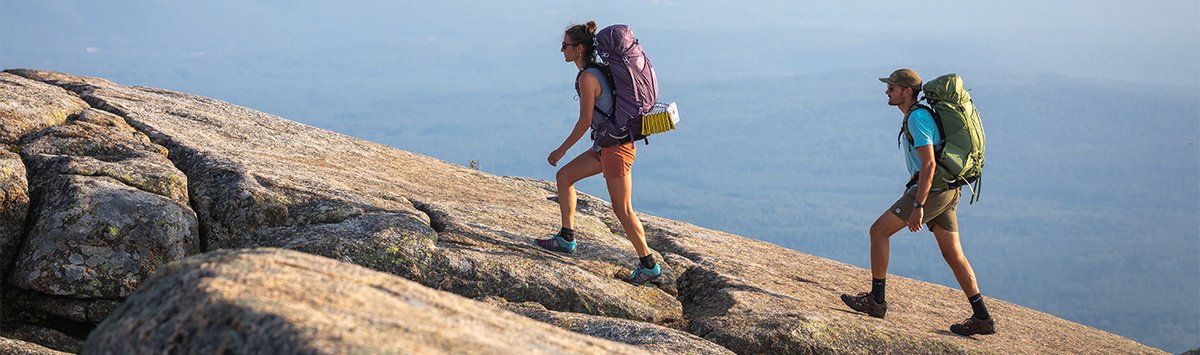 Two backpackers walk up a steep rocky incline.