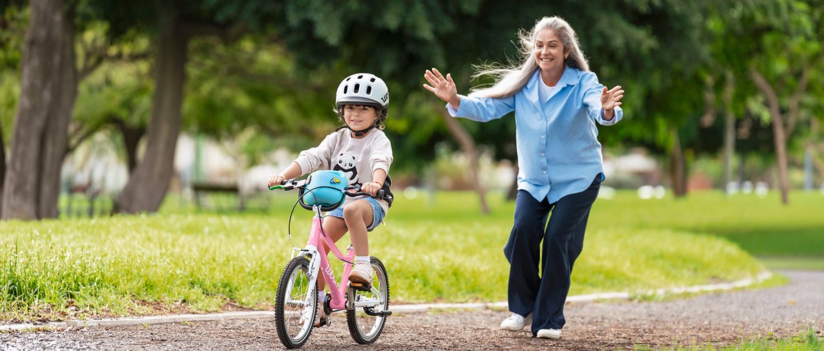 Parent watching younk kid wearing helmet take off on their Woom Go bike.