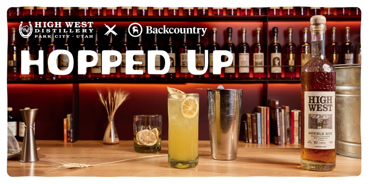 A bar countertop displays a tall cocktail garnished with dried lemon slices, a glass with more lemon slices, a bottle of High West Double Rye, a cocktail shaker, a jigger, wheat stalks, and books, all set against shelves filled with liquor bottles. Bold text at the top reads "Hopped up," with the High West Distillery and Backcountry logos.