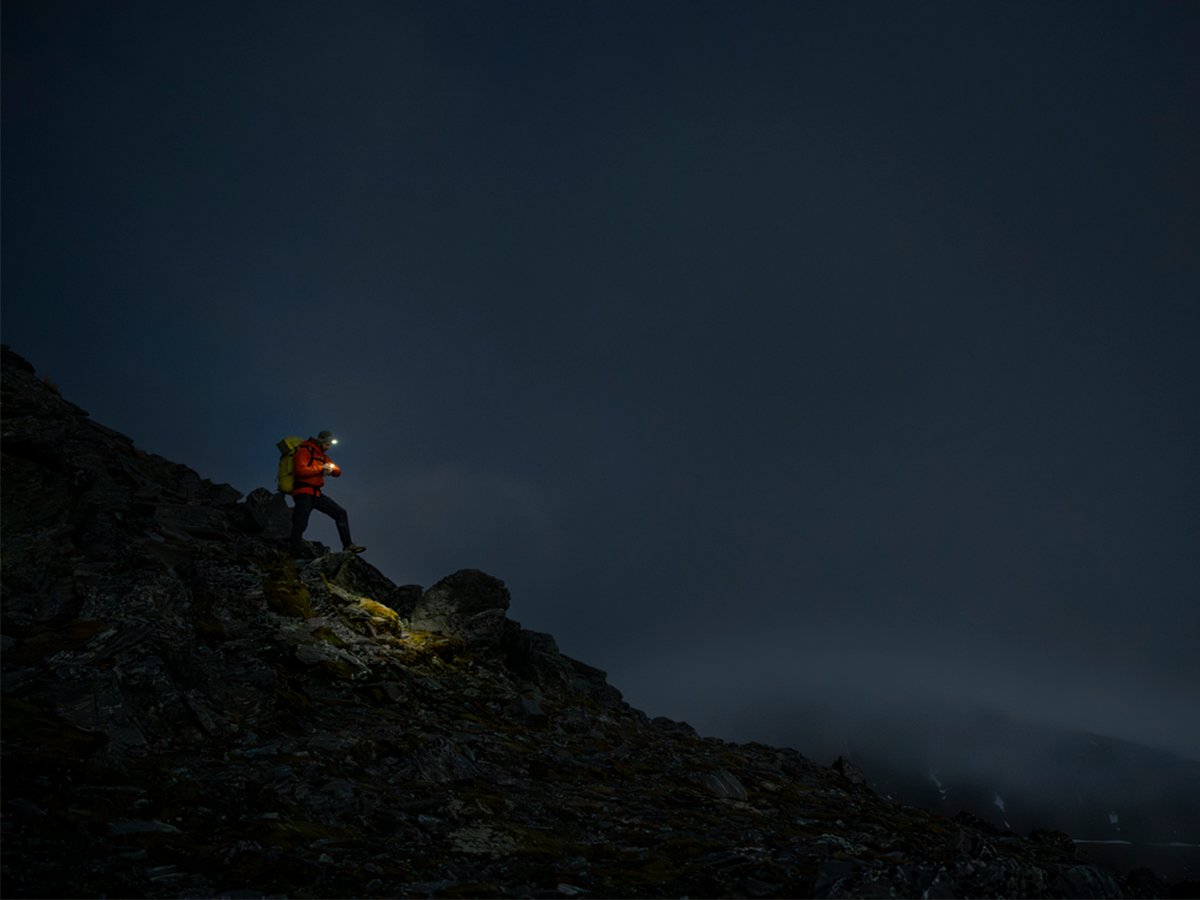 A person wearing a headlamp pauses on a rocky ridge, illuminated against the dark sky.