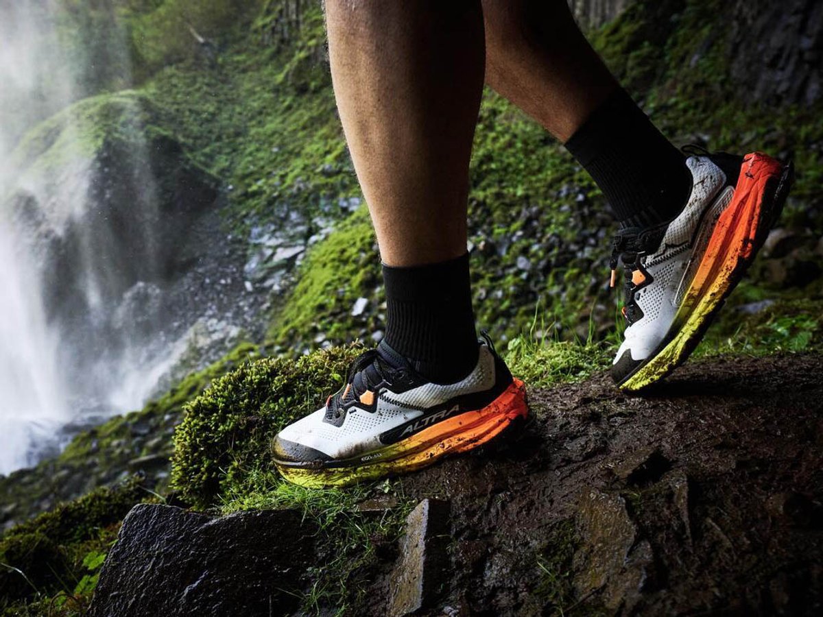 Close up of person standing on mosy patch in fron of waterfall wearing Altra trail shoes.
