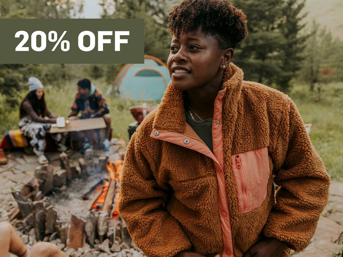 A woman stands in front of a campfire.  A promotional flag says 20% off in the top right corner.