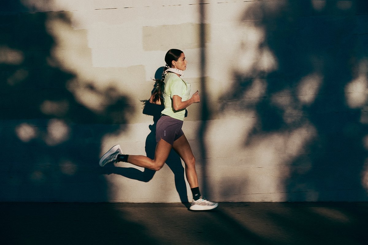 Runner between shadows with buiilding wall behind her. 