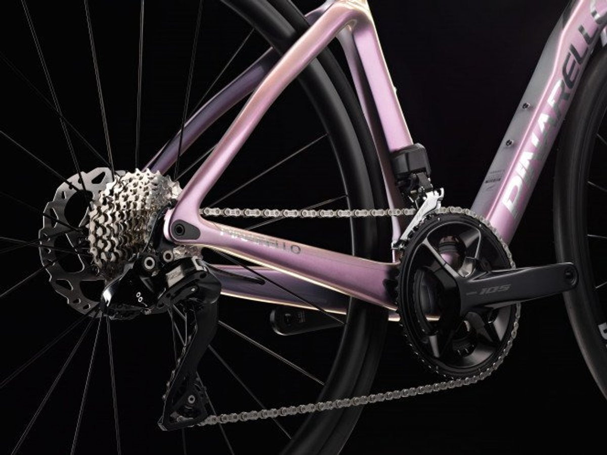 Close-up of iridescent pink Pinarello carbon road bike rear cassette, chain, and crankset against dark background