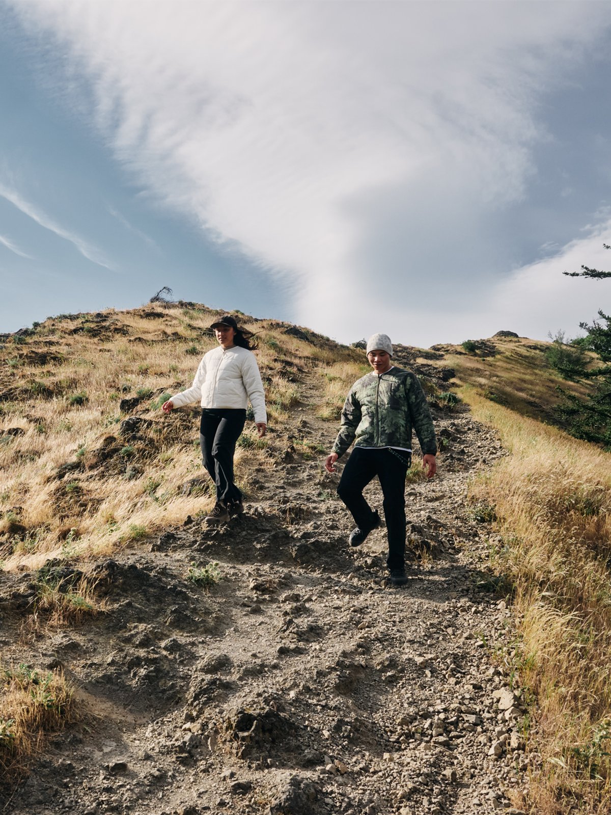 A man and a woman hike down a rocky incline, wearing The North Face puffers.