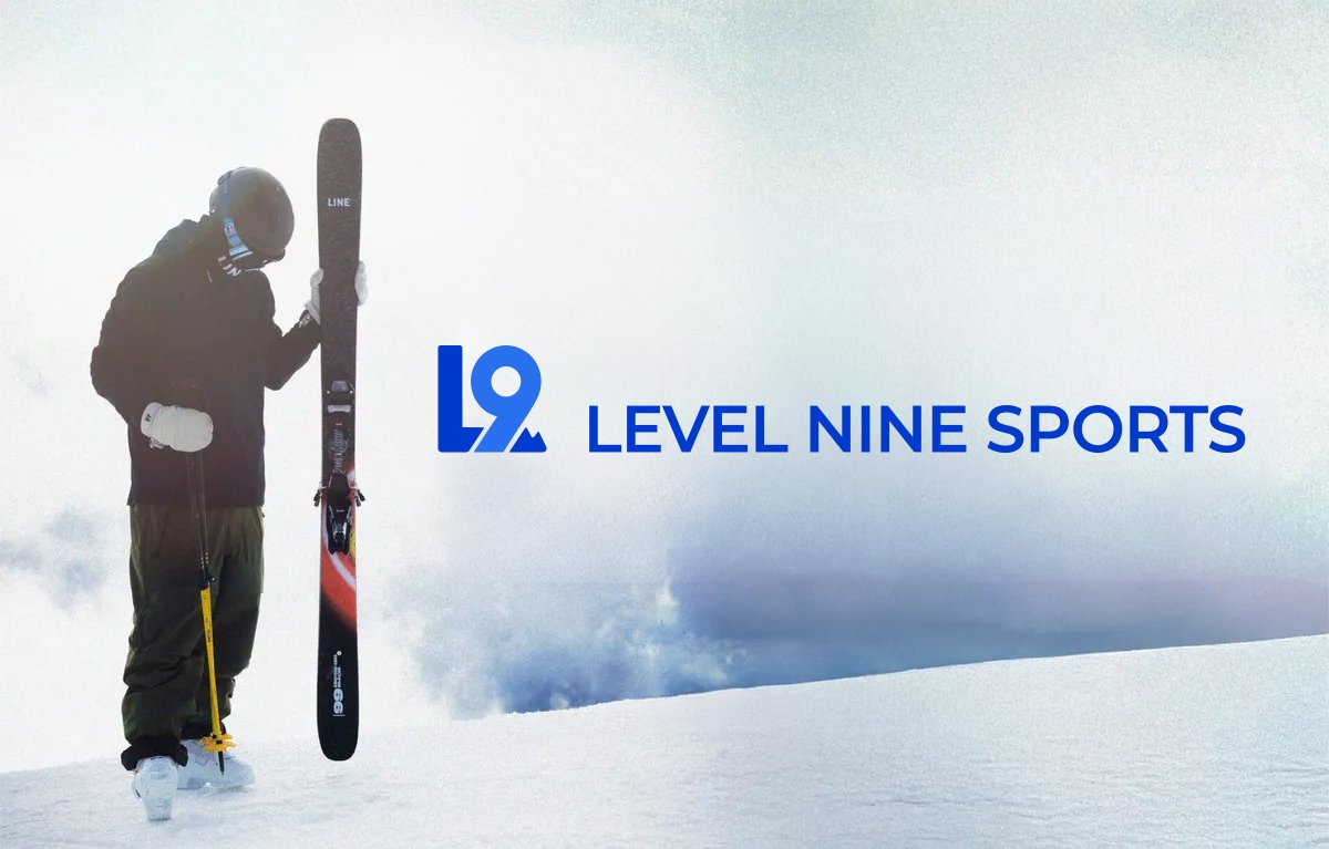 A skier holding a Line brand ski stands in snowy alpine terrain with mountain views, representing Level Nine Sports outdoor gear.
