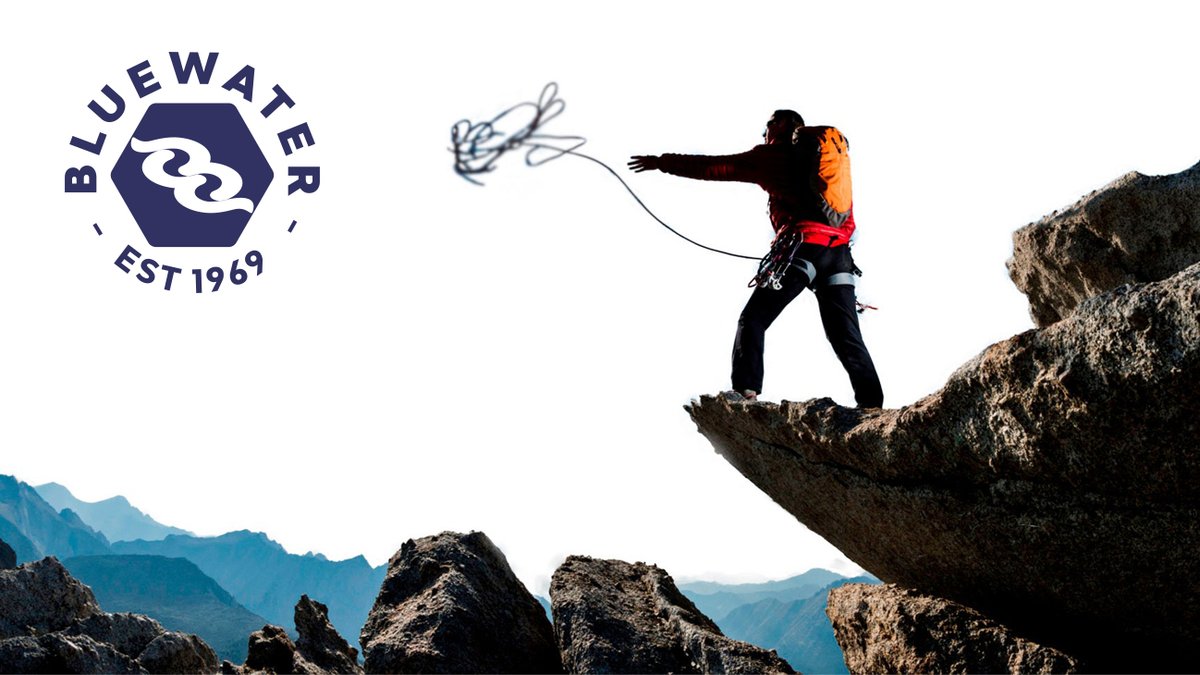 A climber in orange and black gear throws a BlueWater rope while rappelling down a rocky cliff face with misty mountains visible in the background.