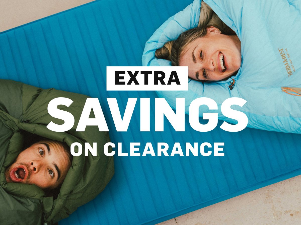 Extra savings on clearance — two campers making silly faces in sleeping bags on a blue Therm-a-Rest sleeping pad.