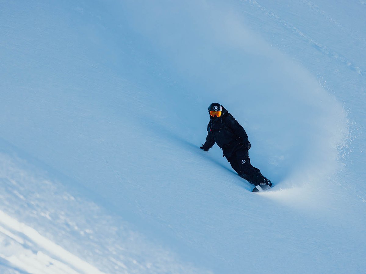 Snowboarder descending a steep slope on toe edge.