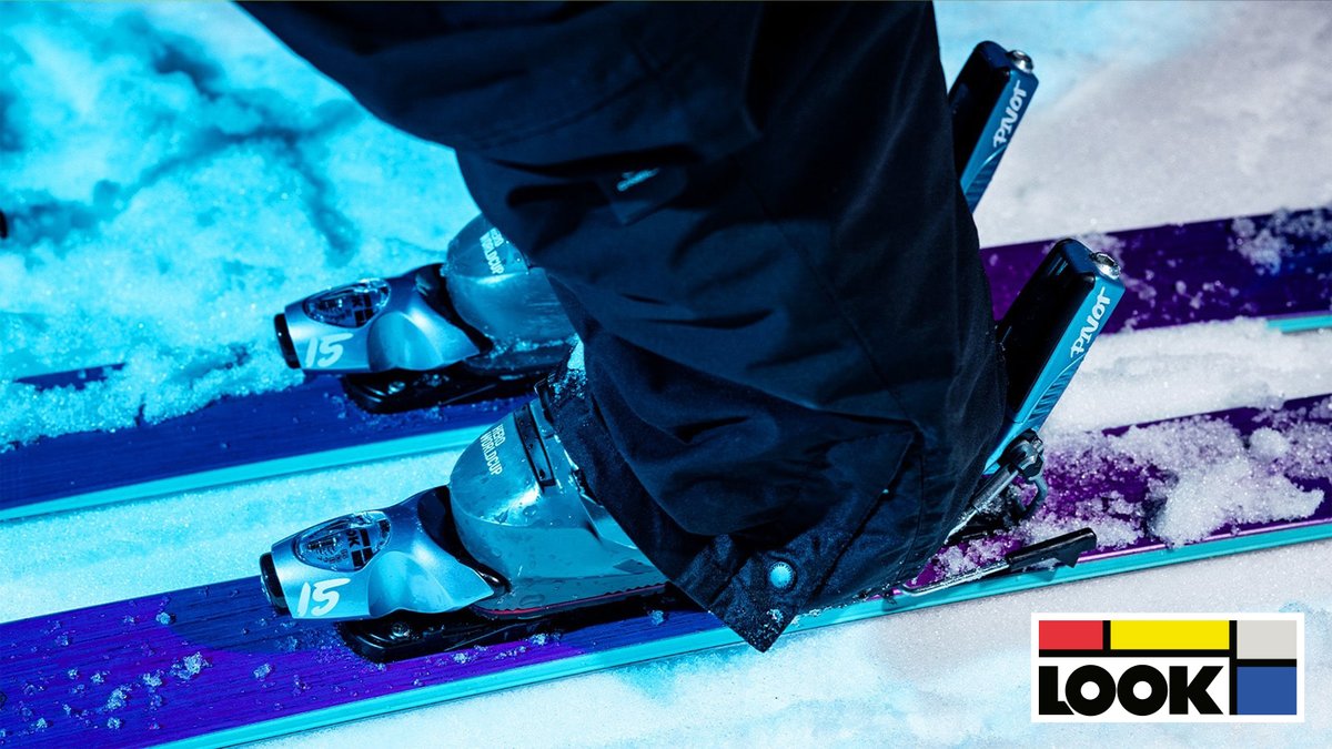 Close-up of ski boots attached to blue and purple skis in snowy conditions, showcasing winter sports equipment for alpine skiing.