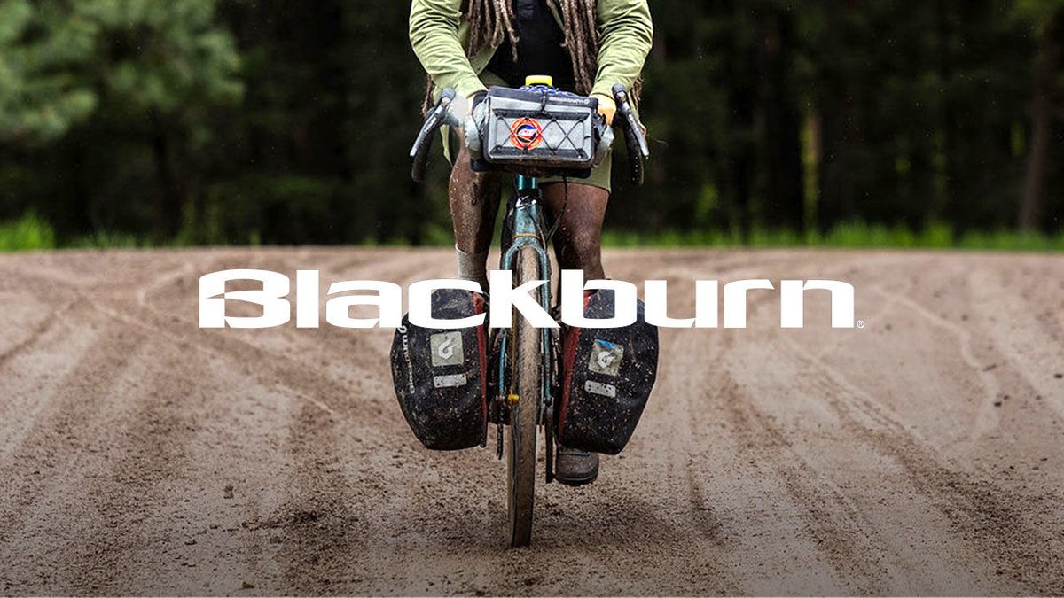 A cyclist rides a gravel bike on a dusty trail wearing a Blackburn handlebar bag, demonstrating adventure cycling gear for outdoor exploration.
