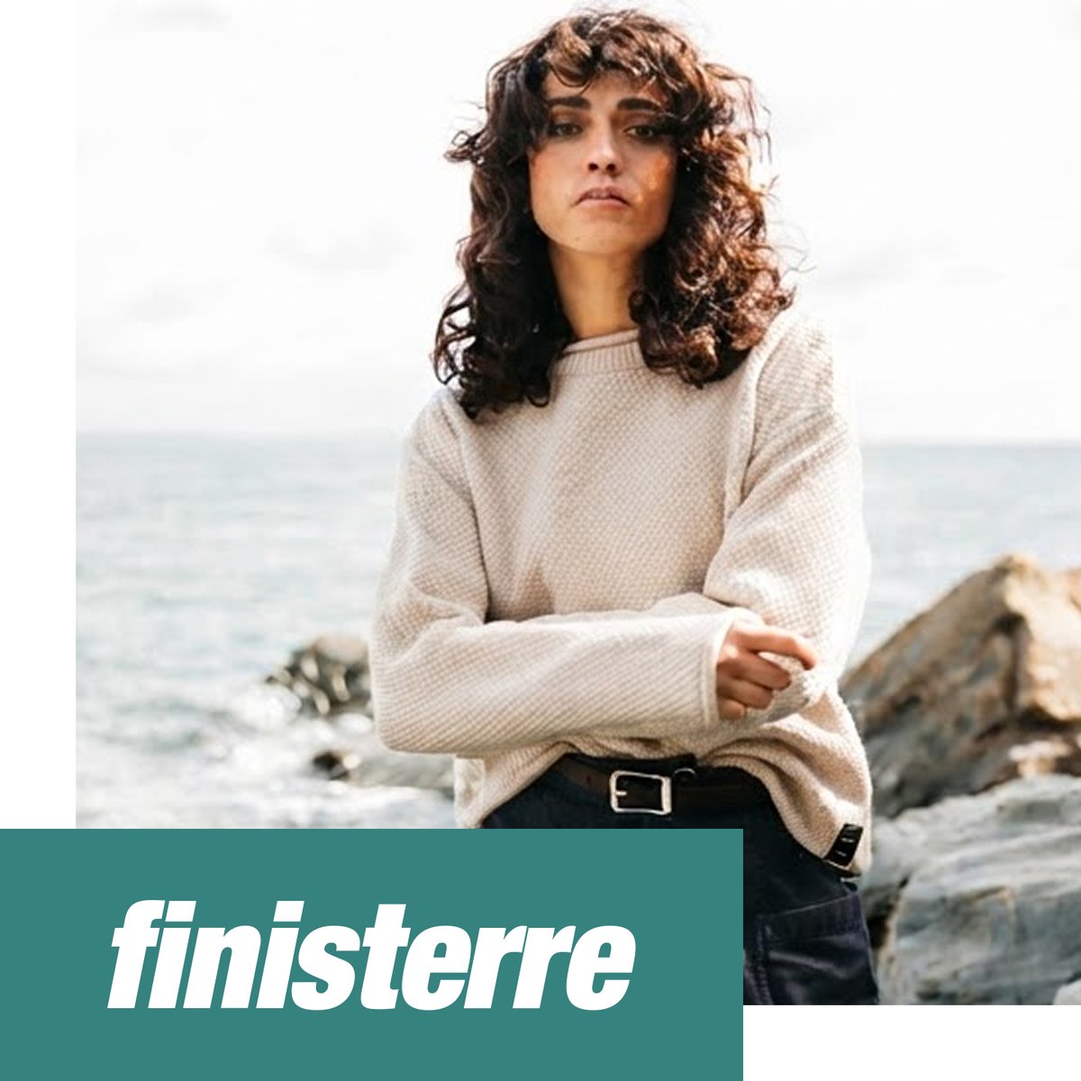Shop Finisterre — woman in a cream knit sweater standing on a rocky coastline.
