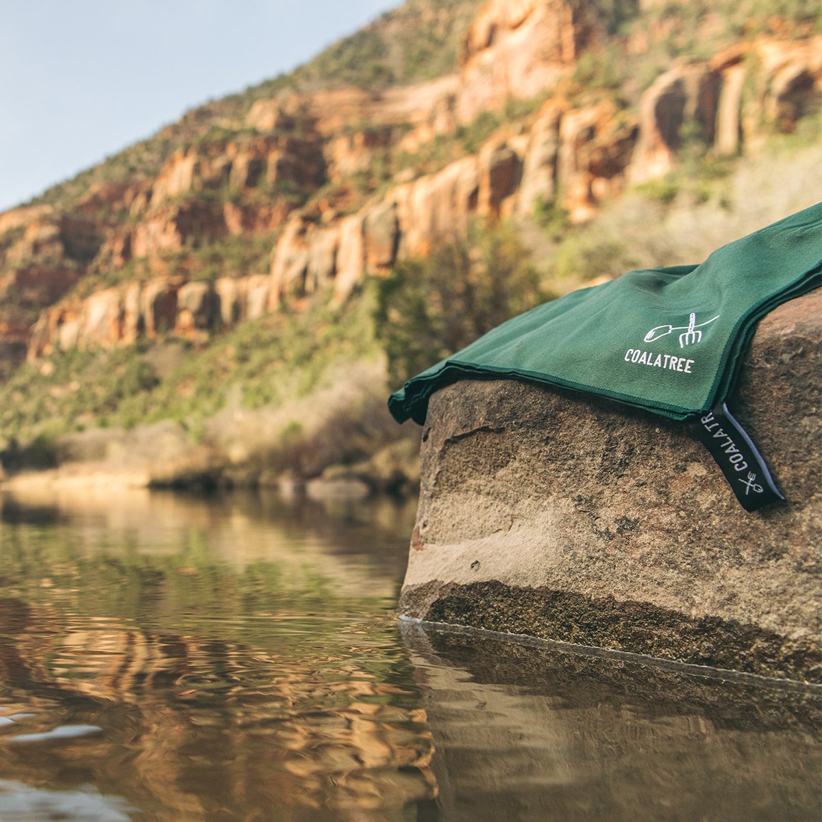 Coalatree Microfiber Towel folded on top of a rock in the middle of a river.