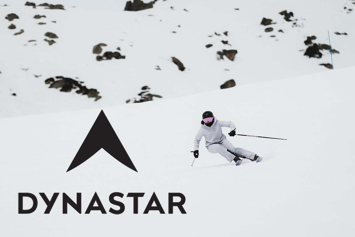 Skier carving on snowy slope with Dynastar logo on alpine mountain background