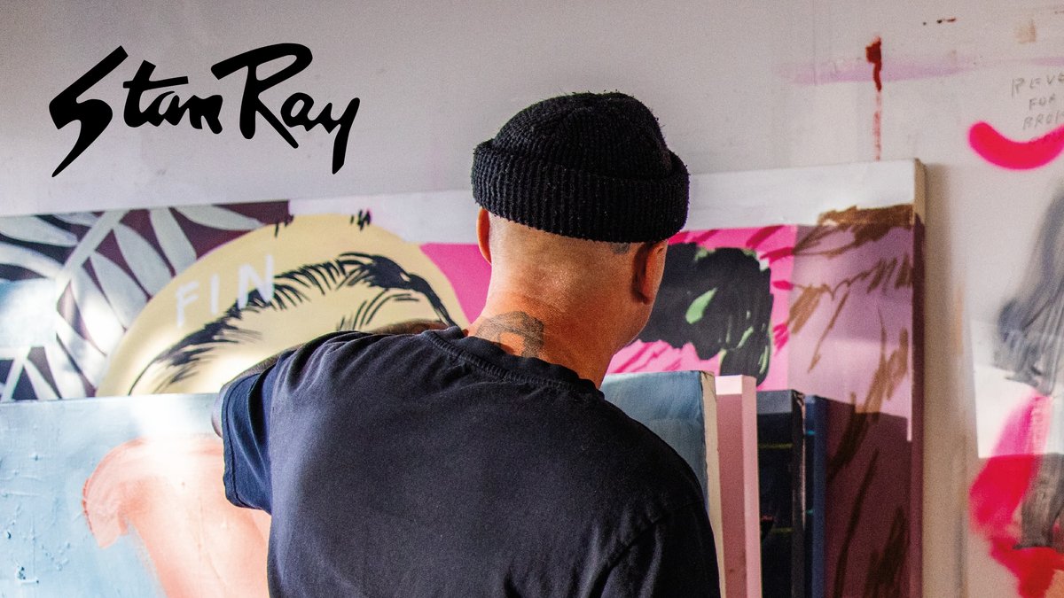 Stan Ray artist working on a vibrant mural featuring bold pink and navy geometric designs with tropical leaf patterns.