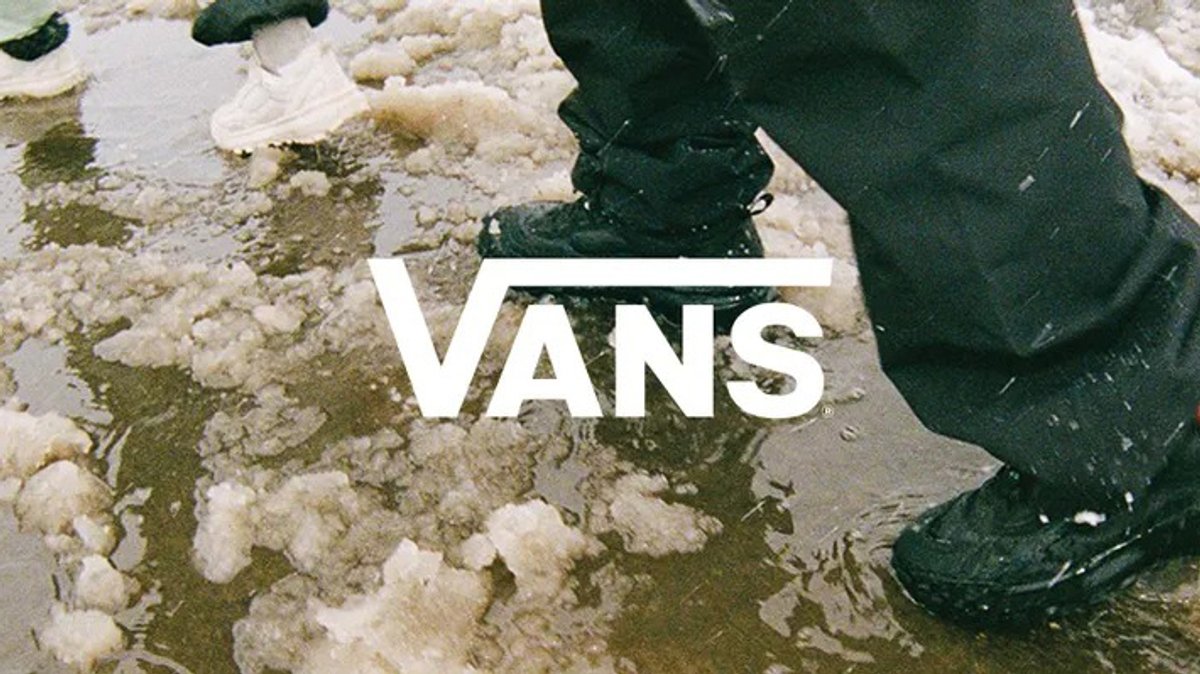 A close-up of heavy-duty black boots walking through slushy snow and mud with a white Vans logo overlaid.