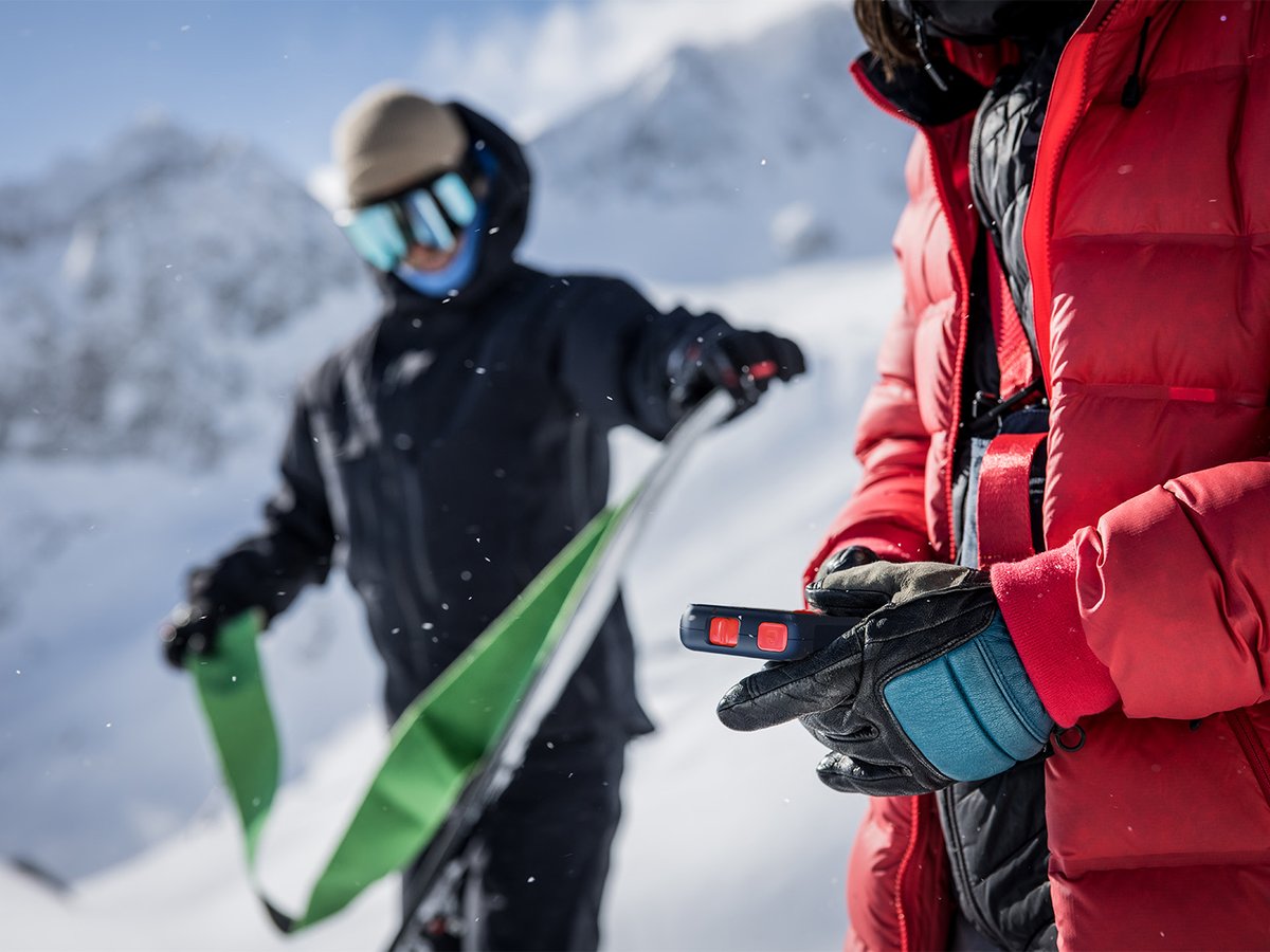 Skier in red holding a Nivia 3D Finder while a partner preps skis.