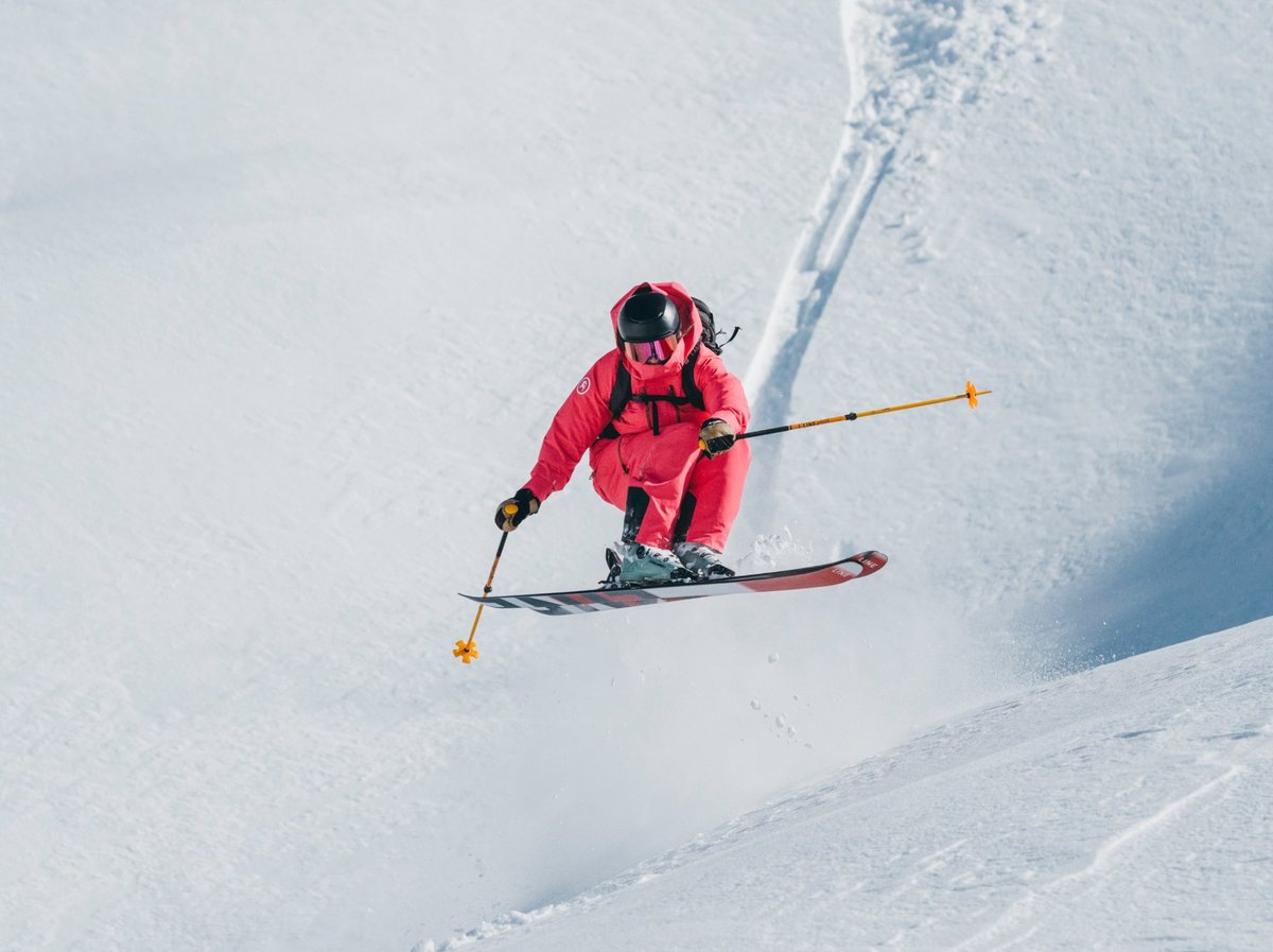 Skier in a red suit catching air into a steep open snowfield.