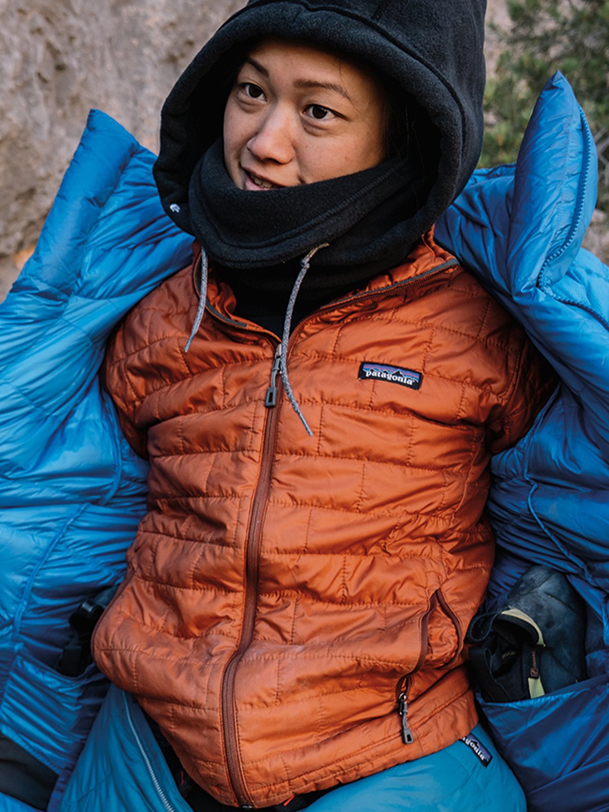 A hiker, wearing a red zip-up Patagonia fleece jacket with a light gray chest pocket, stands outdoors in a sunlit, wooded area.