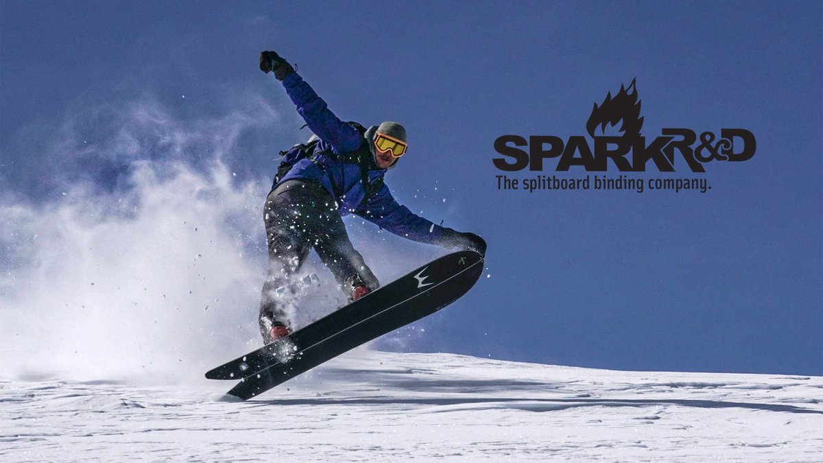 Professional splitboarder in blue jacket performing aerial trick on snowy mountain with Spark R&D splitboard binding company branding displayed.