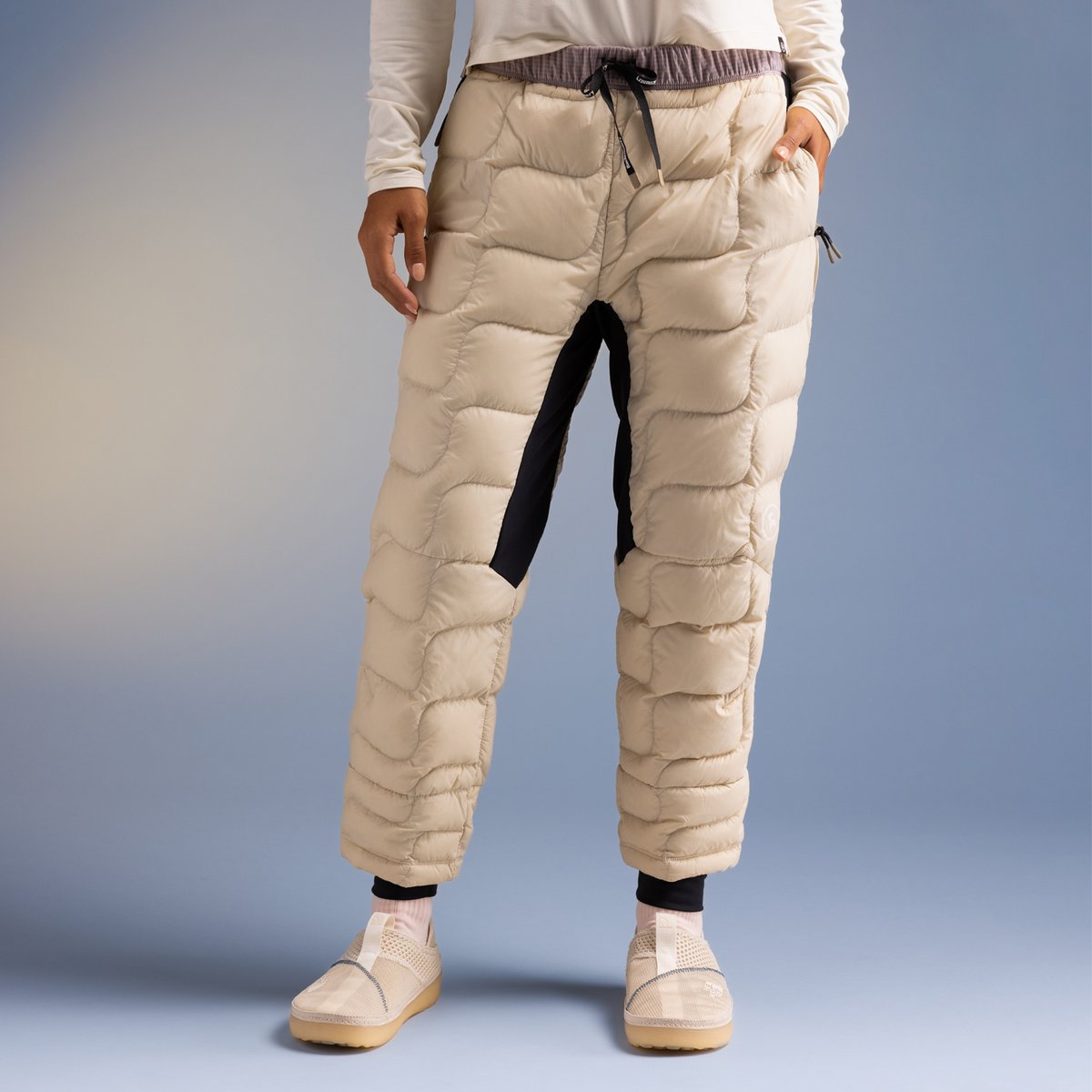Beige quilted puffer pants with black contrast inseam and drawstring waistband, styled with cream long-sleeve top and platform sneakers.