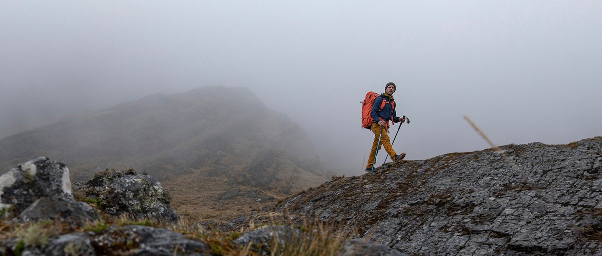 Person hiking along misty mountain ridge wearing Coalatree Whistler Windbreaker.