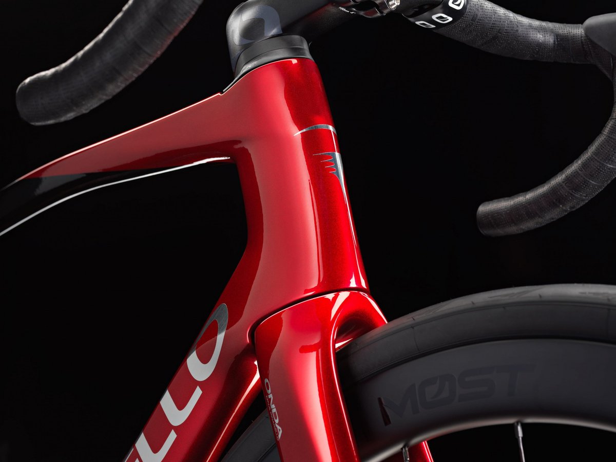 Pinarello red carbon road bike headtube and fork crown junction detail with integrated stem and drop handlebars against dark studio background