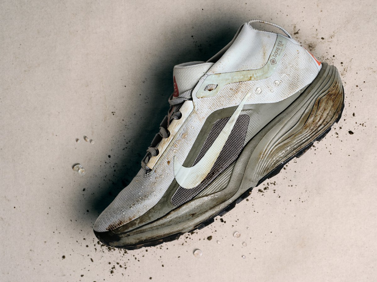 Side view of Nike ACG Pegasus GTX trail shoe with dirt and water drops sitting on white background.