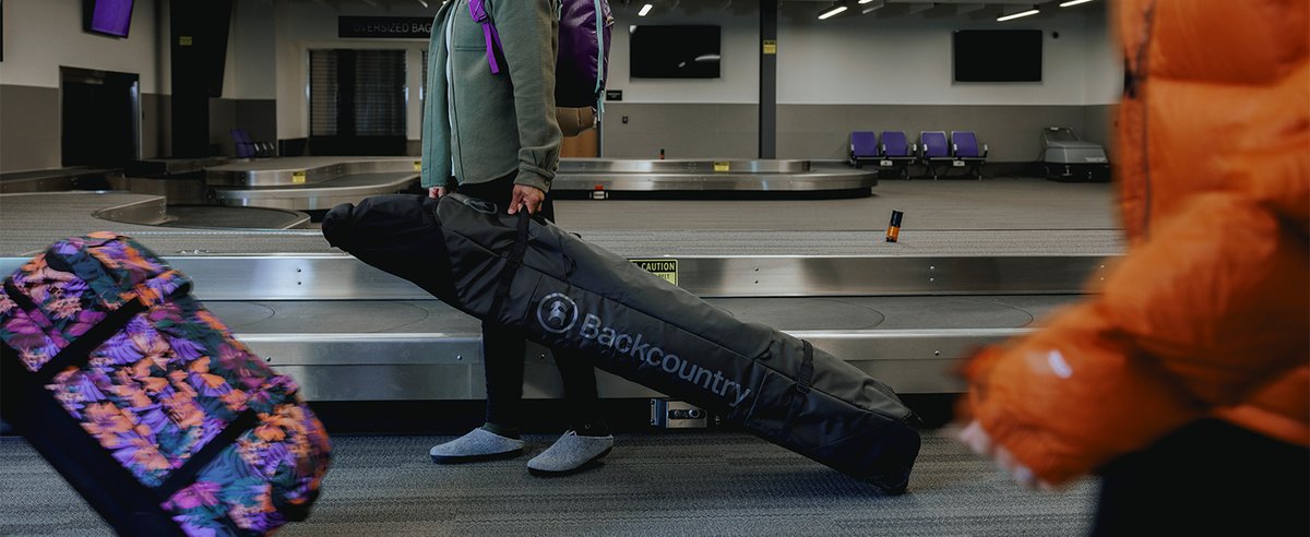 Person wheeling Backcountry Ski Bag at an airport next to baggage claim.
