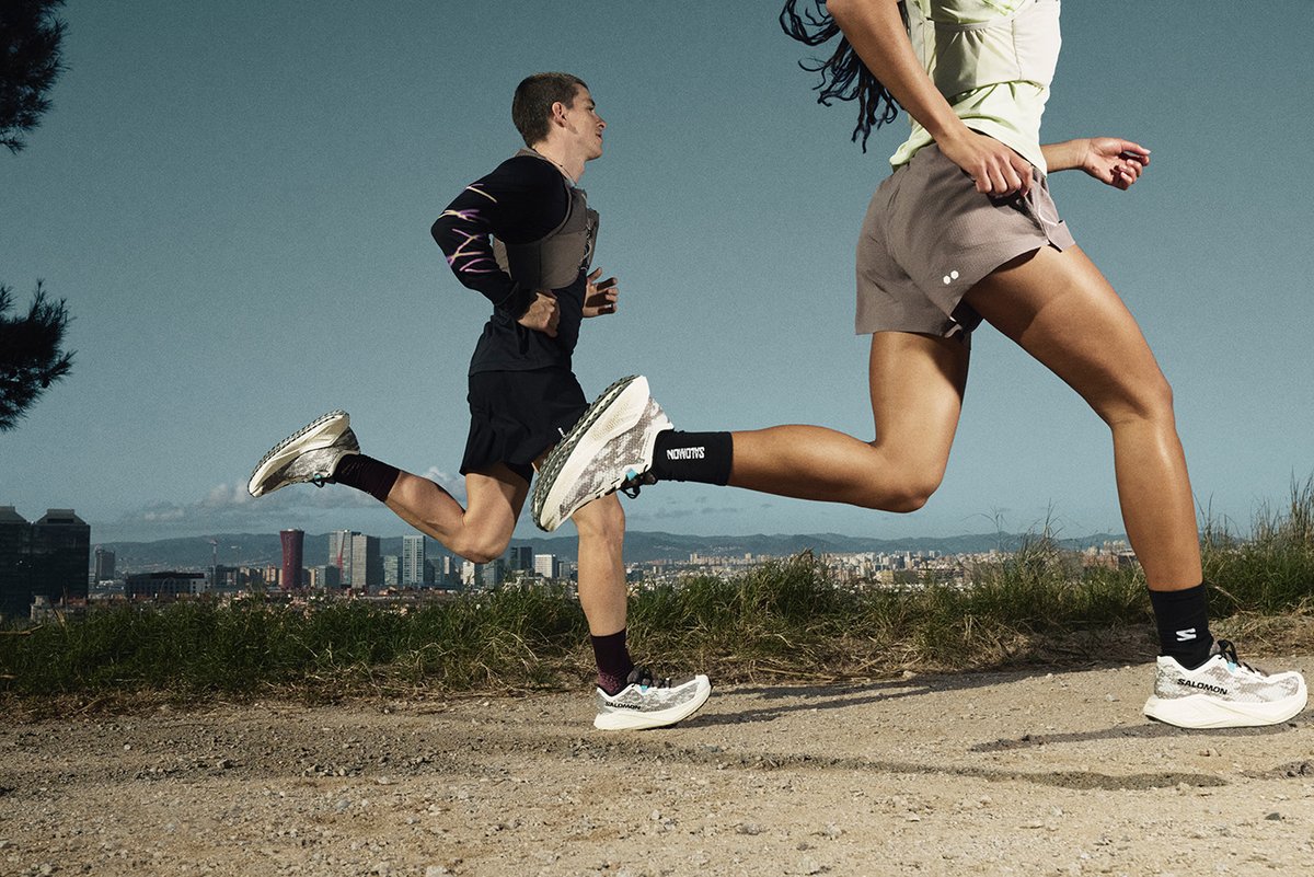 Two runners running on pavement with a city in the background.