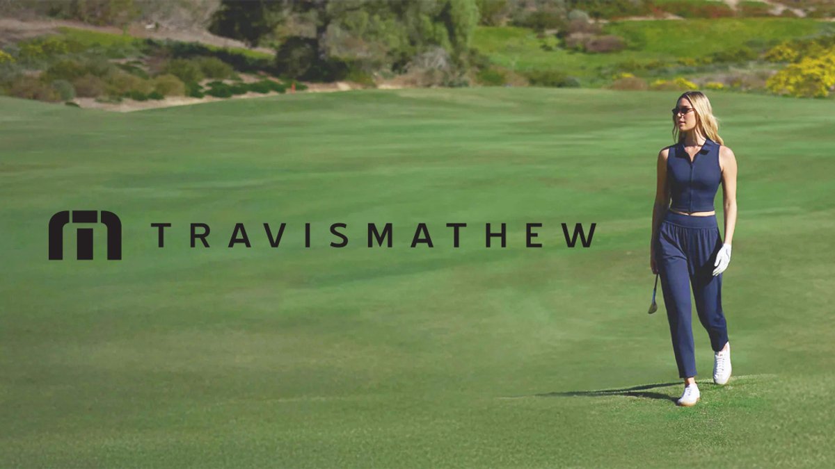 A woman in navy athletic wear stands on a manicured golf course with the Travis Mathew logo displayed beside her.