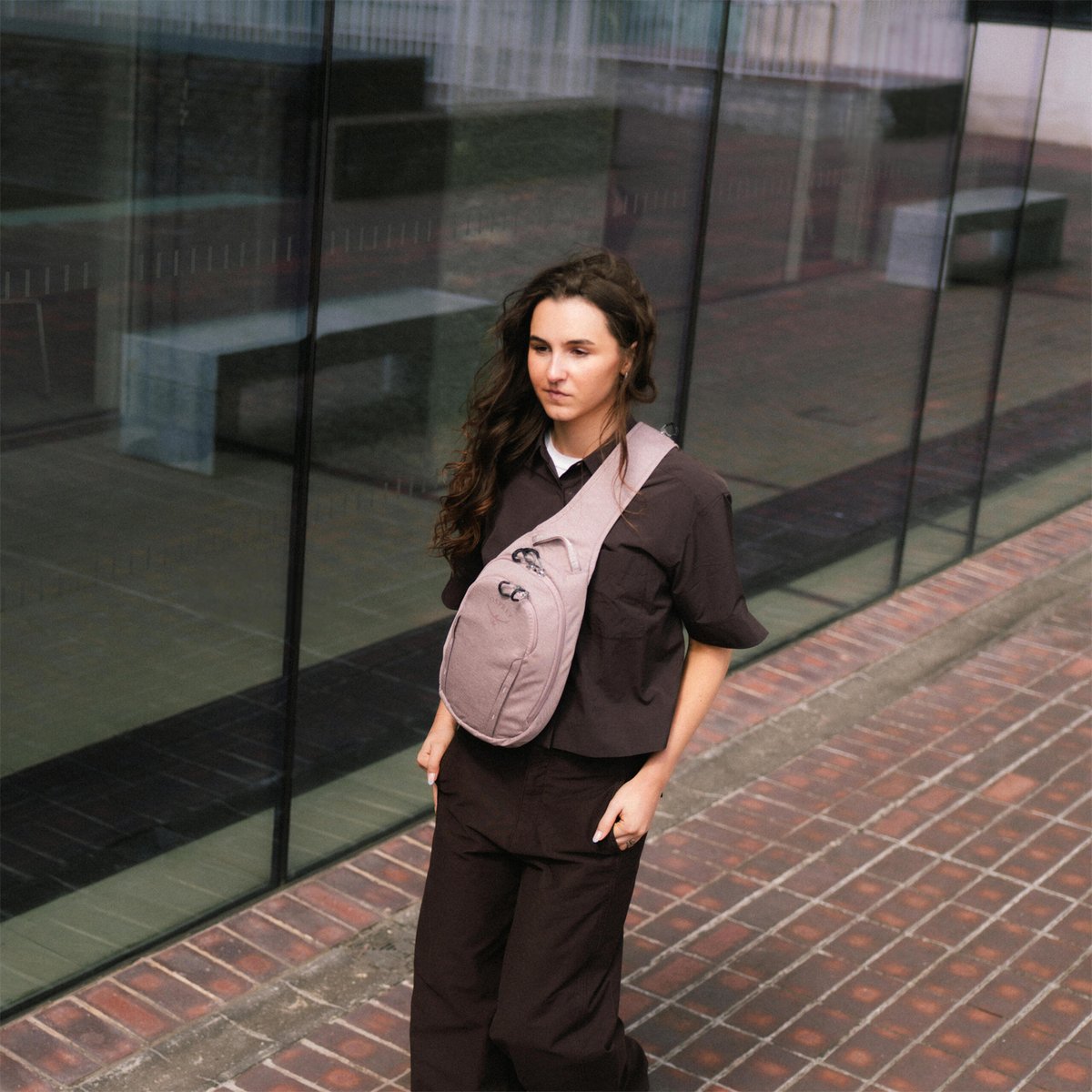 A woman wearing an Osprey Daylite sling walks down a city street. 