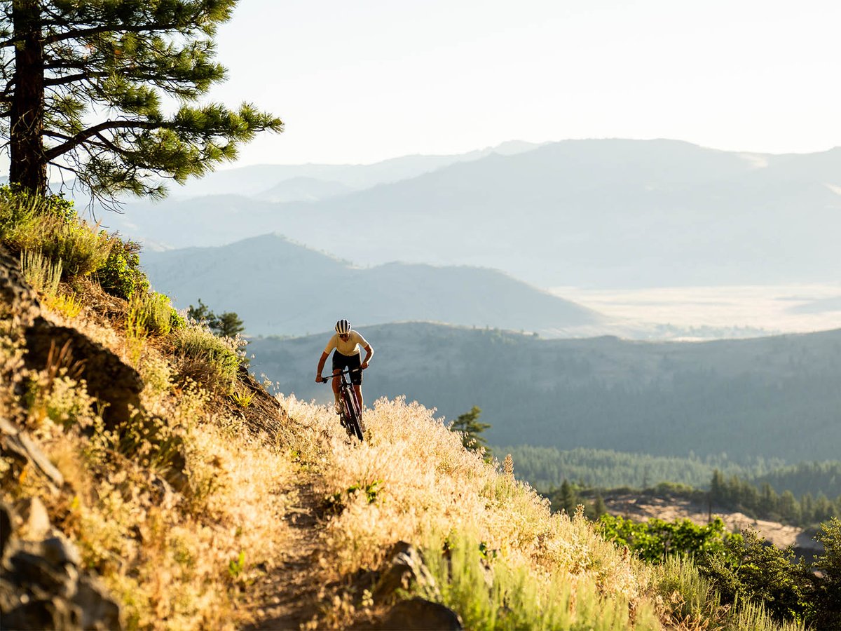 Lone biker riding trail around hillside with mountain view in the background.