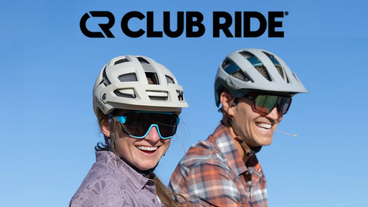 Two smiling cyclists wearing white helmets and sunglasses against a blue sky with the Club Ride logo displayed above them.