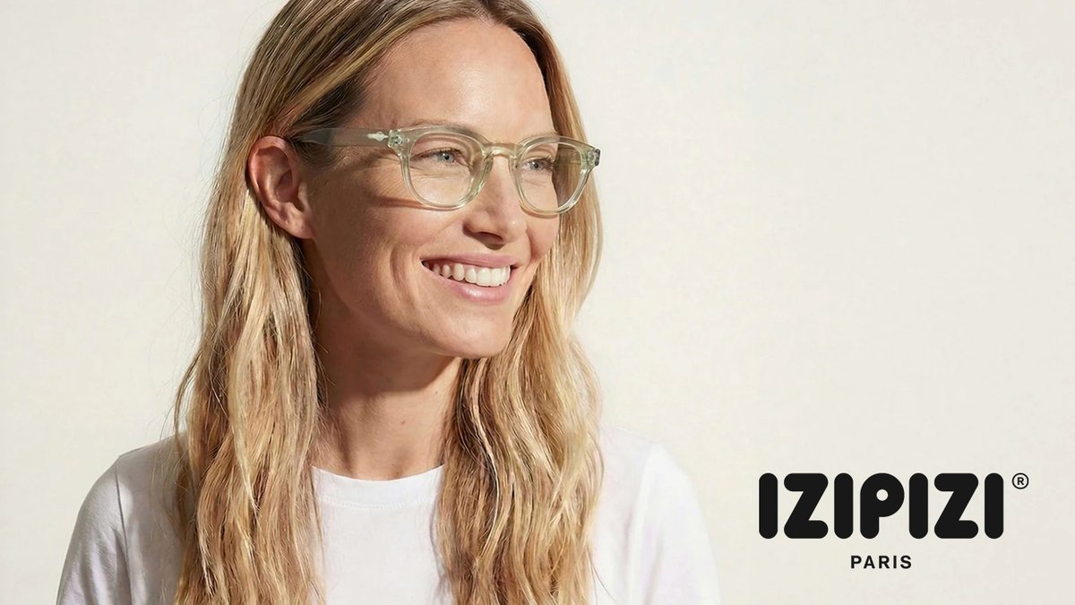 Woman wearing clear frame glasses and a white t-shirt smiling at the camera with IZIPIZI Paris eyewear branding visible.