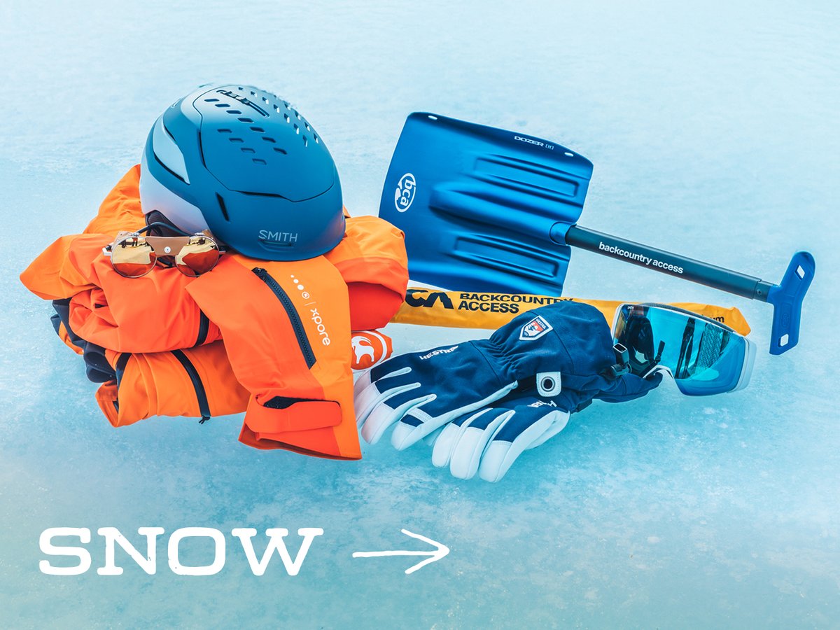 Snow gear, including a helmet, orange shell jacket, gloves, goggles, glacier glasses, and an avalanche shovel, laid out on ice: “Snow.”