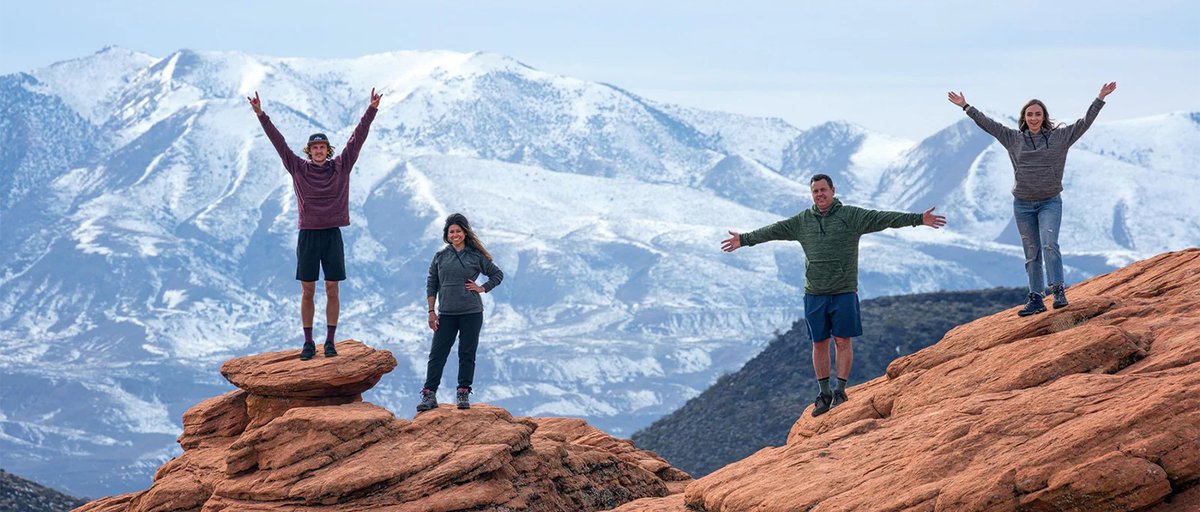 Four people standing on desert ledge with mountains in the background.