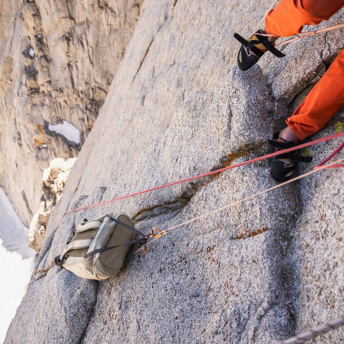 Rock climber wearing climbing shoes hauling gear pack up granite wall on multi pitch alpine trad climb.