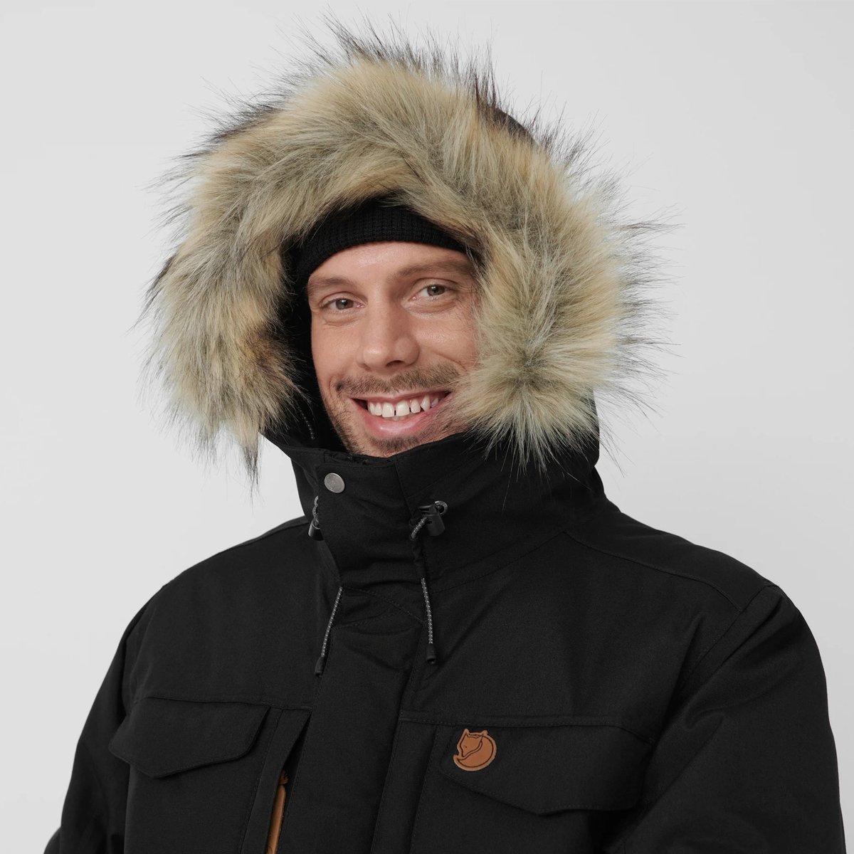 A man wears the Fjallraven Nuuk Parka with the hood up, faux fur haloing his head.